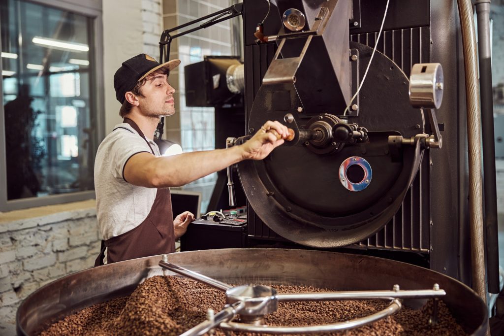 Handsome young man using industrial coffee roasting machine