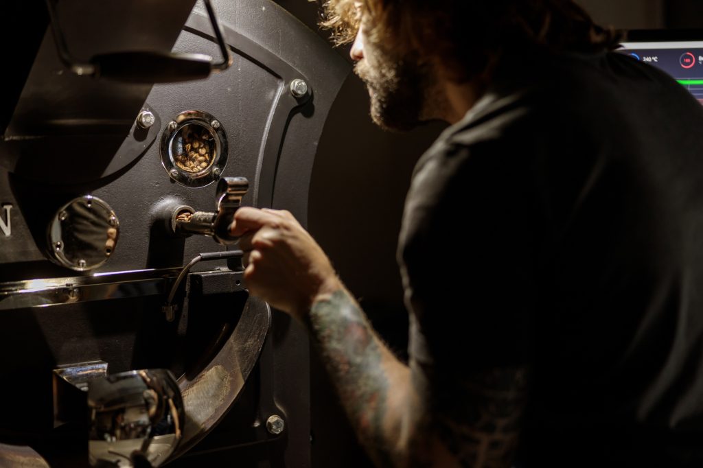 Bearded man using coffee roasting machine at factory