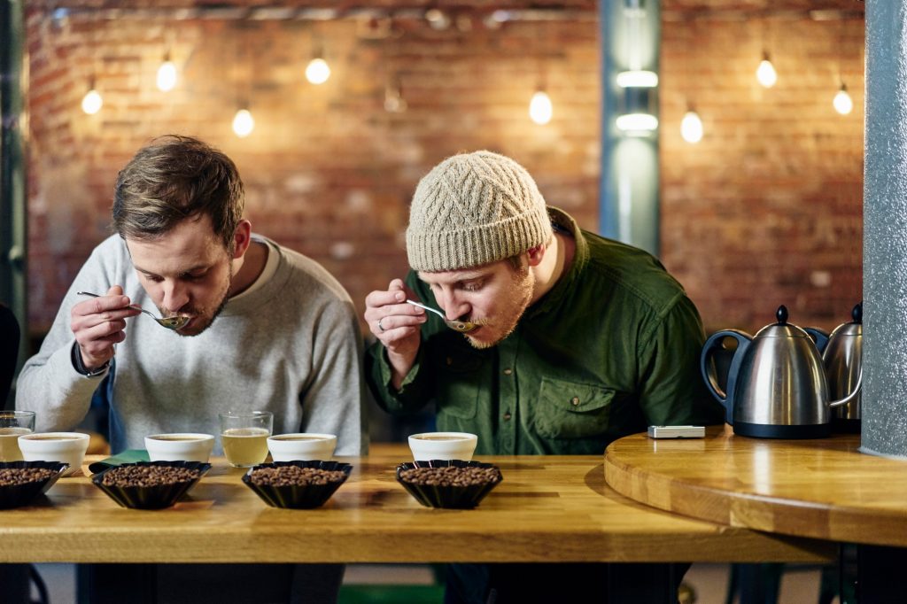 Coffee shop team slurping bowls of coffee and coffee beans at tasting