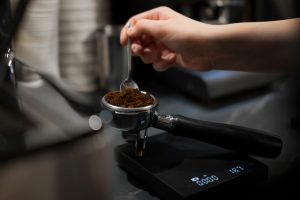 A barista meticulously fills a portafilter with ground coffee, taking care to ensure the correct mea