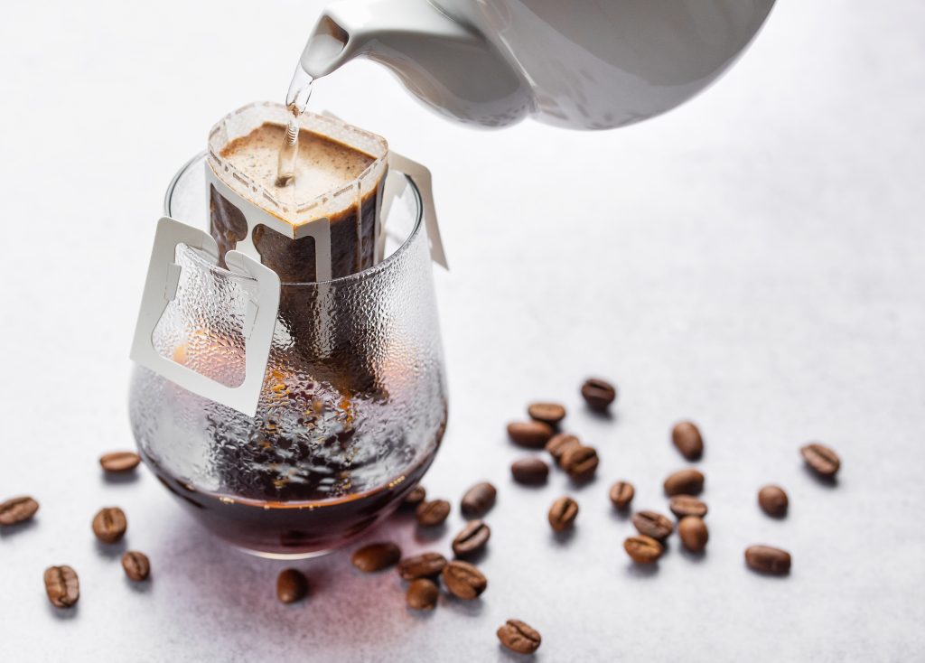 Pouring water into ground coffee, coffee drip bag and glass
