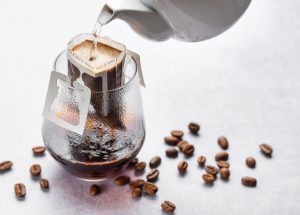 Pouring water into ground coffee, coffee drip bag and glass